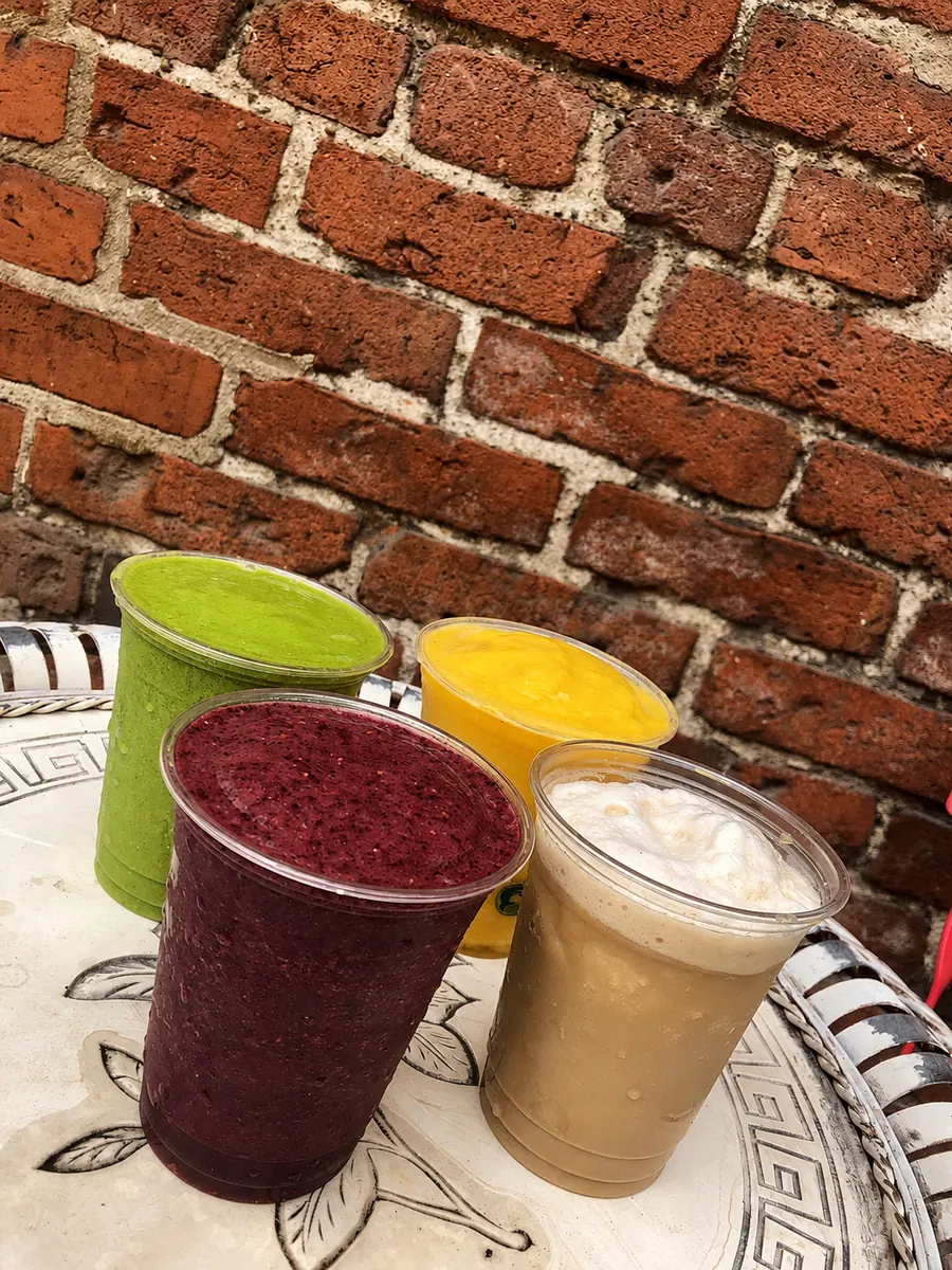 Four colourful smoothies and iced coffee against the deli brick wall